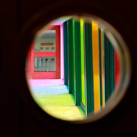 Das Foto gewährt den Blick durch ein in eine Tür eingelassenes rundes Fenster. Dahinter liegt der "Regenbogengang" des Jugendhofs.