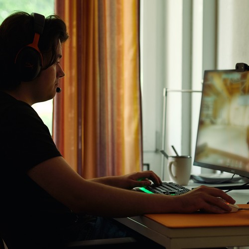 Junger Mann mit Headset sitzt vor PC-Bildschirm und spielt