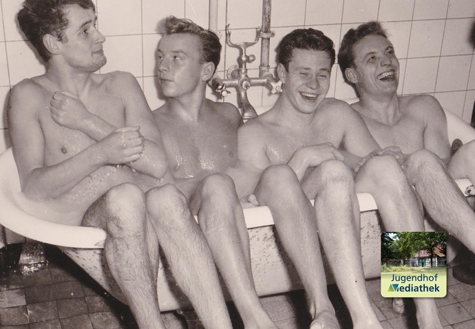Schwarz-weiß-Fotografie aus den 1950er-Jahren. Zu sehen sind vier junge Männer, die seitlich nebeneinander in einer Badewanne sitzen